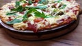 Tasty vegetarian pizza with olives, arugula, mozzarella and cherries on a wooden table.