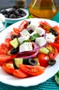 Tasty  vitamin salad with fresh vegetables, feta, black olives, basil sauce on a white plate on a wooden background Royalty Free Stock Photo