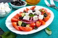 Tasty  vitamin salad with fresh vegetables, feta, black olives, basil sauce on a white plate on a wooden background Royalty Free Stock Photo