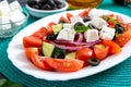 Tasty  vitamin salad with fresh vegetables, feta, black olives, basil sauce on a white plate on a wooden background Royalty Free Stock Photo