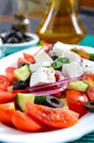 Tasty  vitamin salad with fresh vegetables, feta, black olives, basil sauce on a white plate on a wooden background Royalty Free Stock Photo