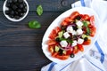 Tasty  vitamin salad with fresh vegetables, feta, black olives, basil sauce on a white plate on a wooden background. Top view Royalty Free Stock Photo