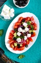 Tasty  vitamin salad with fresh vegetables, feta, black olives, basil sauce on a white plate on a wooden background. Top view Royalty Free Stock Photo