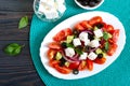 Tasty  vitamin salad with fresh vegetables, feta, black olives, basil sauce on a white plate on a wooden background. Top view Royalty Free Stock Photo