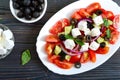 Tasty  vitamin salad with fresh vegetables, feta, black olives, basil sauce on a white plate on a wooden background. Top view Royalty Free Stock Photo