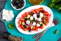 Tasty  vitamin salad with fresh vegetables, feta, black olives, basil sauce on a white plate on a wooden background. Top view Royalty Free Stock Photo