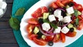 Tasty  vitamin salad with fresh vegetables, feta, black olives, basil sauce on a white plate on a wooden background. Top view Royalty Free Stock Photo