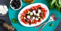 Tasty  vitamin salad with fresh vegetables, feta, black olives, basil sauce on a white plate on a wooden background. Top view Royalty Free Stock Photo