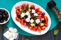 Tasty  vitamin salad with fresh vegetables, feta, black olives, basil sauce on a white plate on a wooden background. Top view Royalty Free Stock Photo