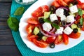 Tasty  vitamin salad with fresh vegetables, feta, black olives, basil sauce on a white plate on a wooden background. Top view. Royalty Free Stock Photo