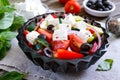 Tasty  vitamin salad with fresh vegetables, goat cheese, black olives, basil sauce on a white plate on a wooden background Royalty Free Stock Photo