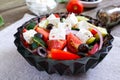 Tasty  vitamin salad with fresh vegetables, goat cheese, black olives, basil sauce on a white plate on a wooden background Royalty Free Stock Photo