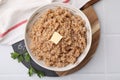 Tasty wheat porridge with butter and parsley in bowl on white tiled table, top view