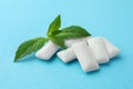 Tasty white chewing gums and mint leaves on light blue background, closeup