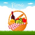 Tasty wicker picnic basket with a bottle of red wine, fruit and cheese on green grass. Royalty Free Stock Photo