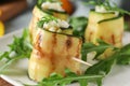 Tasty zucchini rolls with cheese and arugula on plate, closeup