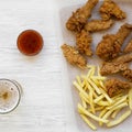 Tasy fast food: fried chicken drumsticks, spicy wings, French fries and chicken strips with sour-sweet sauce and cold beer over Royalty Free Stock Photo