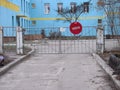 Tattered gate with a no entry sign and a paper note, a blue building and a courtyard