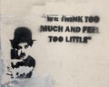 Tattered graffiti with image Charlie Chaplin and part of one of his famous quotes, `We think too much and feel too little`.