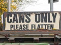 A tattered outside sign at recycling plant and bins saying cans