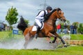 Tattersalls horse show in Ireland, chestnut horse galopping after obstacle in water with male rider, jockey rushing forward