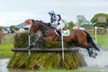 Tattersalls horse show in Ireland, horse jumping over obstacle in water with male rider, jockey rushing flying forward