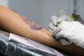 A tattoo artist fills a drawing on a man`s hand with a typewriter. The concept of overcoming pain, courage, creativity and