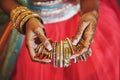 The hand with mehndi of Indian bride holding a lot of glitter bracelets bangle with red legenha background, close-up Royalty Free Stock Photo