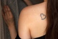 Tattoo of heart on naked female back, young adult woman from behind, closeup of sensual tatoo, candid faceless concept