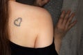 Tattoo of heart on naked female back, young adult woman from behind, closeup of sensual tatoo, candid faceless concept