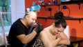 In a tattoo salon , a specialist is doing a tattoo on woman`s back, a floral ornament. a man works in special gloves, on