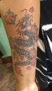 Tattoo on woman of colors arm. Chinese styled dragon in green, red and grey