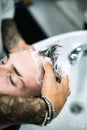 Tattooed barber washing client hair before haircut in barbershop Royalty Free Stock Photo