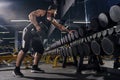 Tattooed, bearded, muscular sportsman in black shorts, vest, cap. Exercising with dumbbells for training his triceps Royalty Free Stock Photo