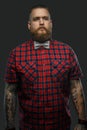 Tattooed bearded unformal male in red shirt and grey bow tie.