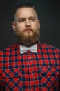 Tattooed bearded unformal male in red shirt and grey bow tie.