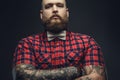 Tattooed bearded unformal male in red shirt and grey bow tie.