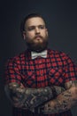 Tattooed bearded unformal male in red shirt and grey bow tie. Royalty Free Stock Photo