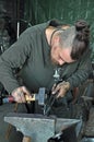 Tattooed blacksmith working with hammer on anvil