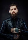 Tattooed cool bearded man in a leather jacket in a dark studio