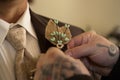 Tattooed hands pin burlap corsage on groom