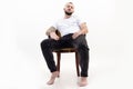 Tattooed handsome brunet, confident, bearded barefoot man sit relaxing like boss on chair like boss. Low angle view