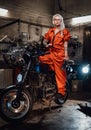 Beautiful female mechanic in orange overalls hold a big wrench and posing for a camera in garage Royalty Free Stock Photo