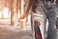 Tattooed hipster girl in torn jeans with a cup of coffee or tea. standing in the park Royalty Free Stock Photo