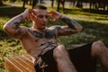 Tattooed man doing sit ups on a park bench