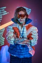 Tattooed racer girl standing over neon vivid text projection in a bright studio holding her glasses, close up look