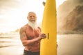 Tattooed senior surfer holding surf board on the beach at sunset - Happy old guy having fun doing extreme sport - Joyful elderly Royalty Free Stock Photo