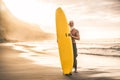 Tattooed senior surfer holding surf board on the beach at sunset - Happy old guy having fun doing extreme sport - Joyful elderly Royalty Free Stock Photo