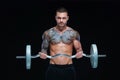 Tattooed strong muscular athletic man pumping up muscles with barbell on black background Royalty Free Stock Photo