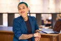 Tattooed woman with electric blue hair sits at desk with laptop